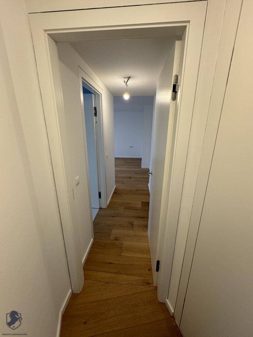 Langer, heller Flur mit Holzboden und weißen Türen, der verschiedene Wohnbereiche verbindet.