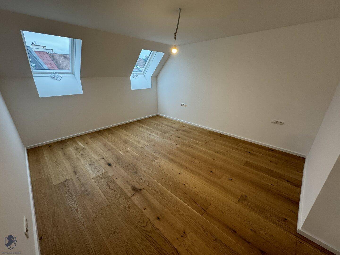 Helles Dachzimmer mit Holzboden, schrägen Wänden und zwei Dachfenstern für viel Tageslicht.