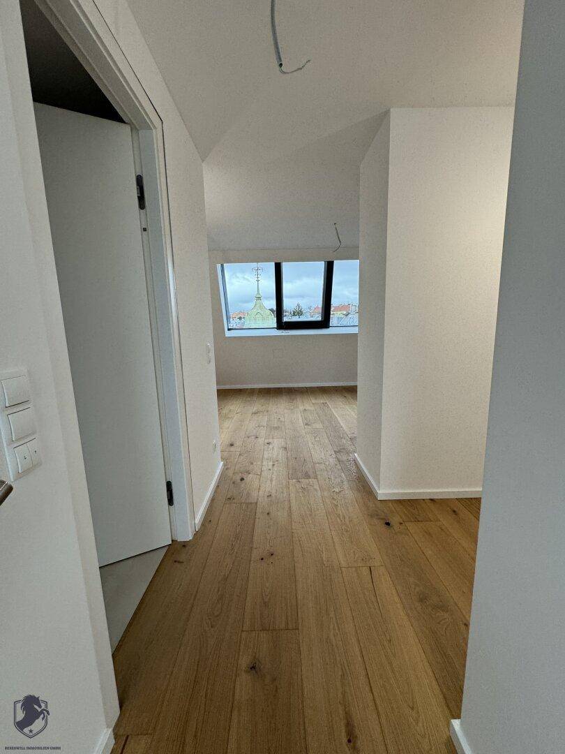 Heller Flur mit Holzboden und Blick in ein weiteres Zimmer mit großem Fenster.