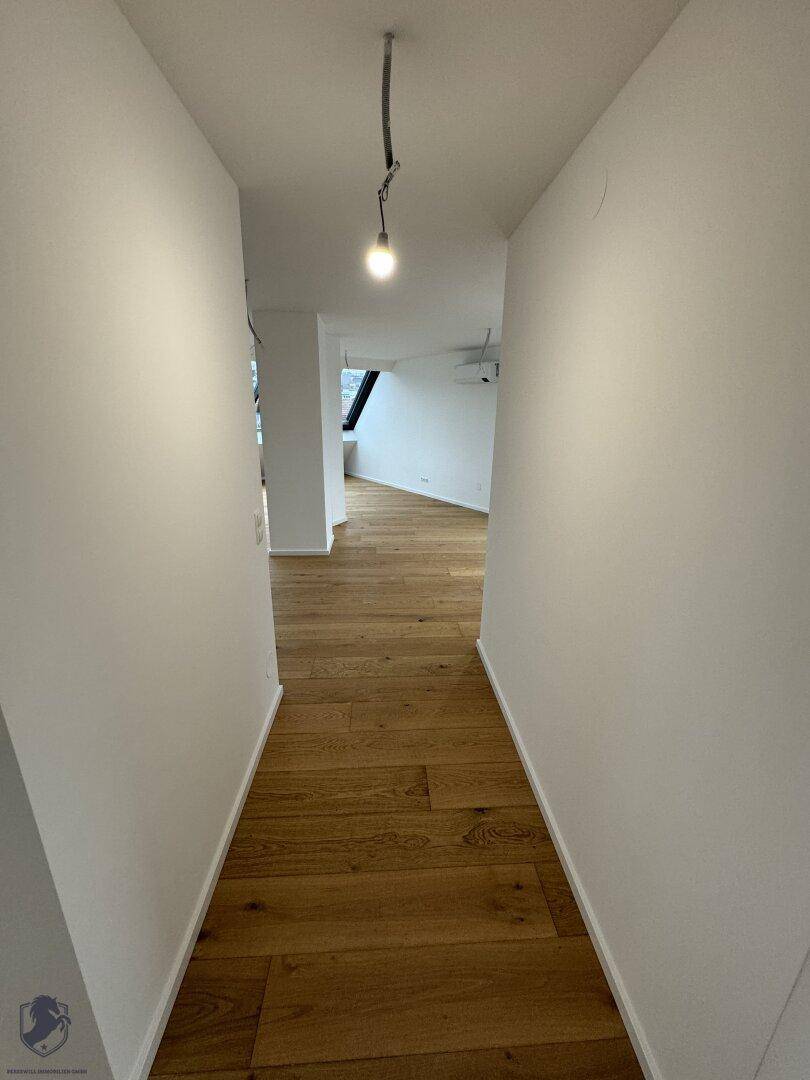 Langer, heller Flur mit Holzboden, der zu einem offenen Wohnbereich im Dachgeschoss führt.
