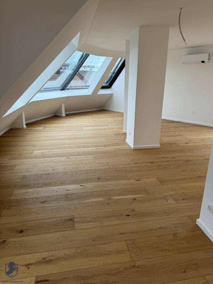Geräumiger Wohnbereich im Dachgeschoss mit Holzboden, schrägen Wänden und Dachfenstern.