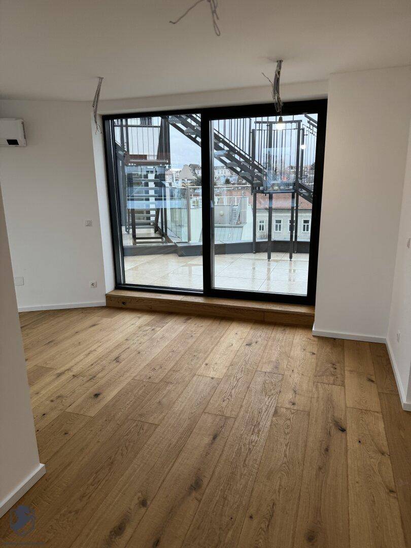 Heller Wohnraum mit Holzboden und großer Glasfront, die Zugang zur Dachterrasse bietet.