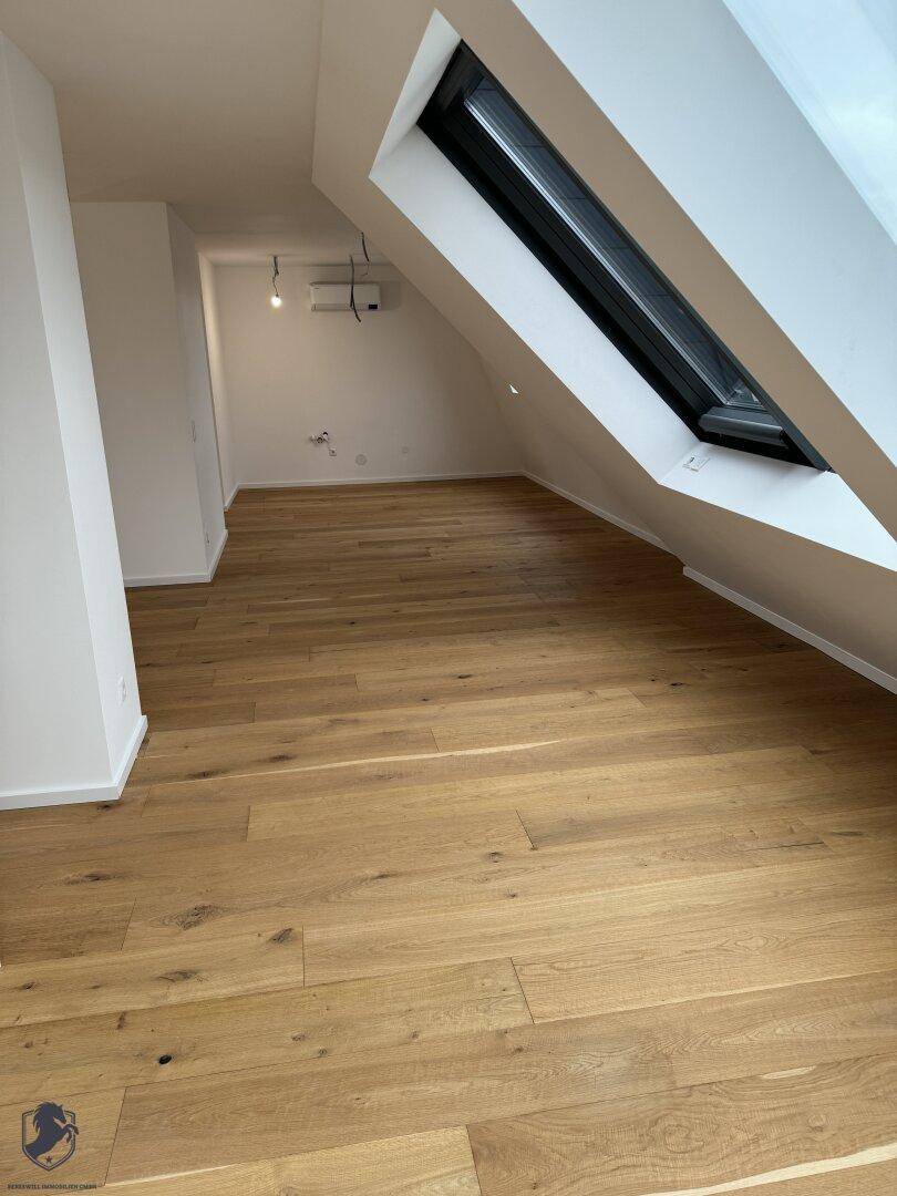 Heller Wohnbereich im Dachgeschoss mit Holzboden, schrägen Wänden und einem großen Dachfenster.