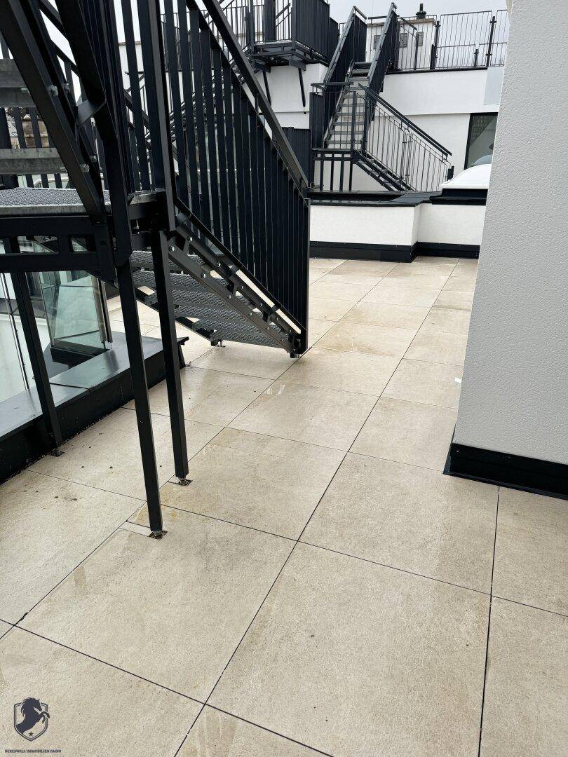 Geräumige Dachterrasse mit hellen Fliesen und einer modernen Metalltreppe.