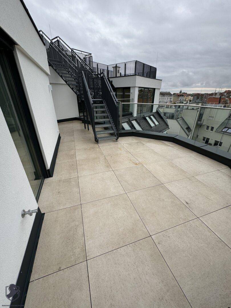 Weitläufige Dachterrasse mit Fliesenboden und Blick über die Dächer der Stadt.