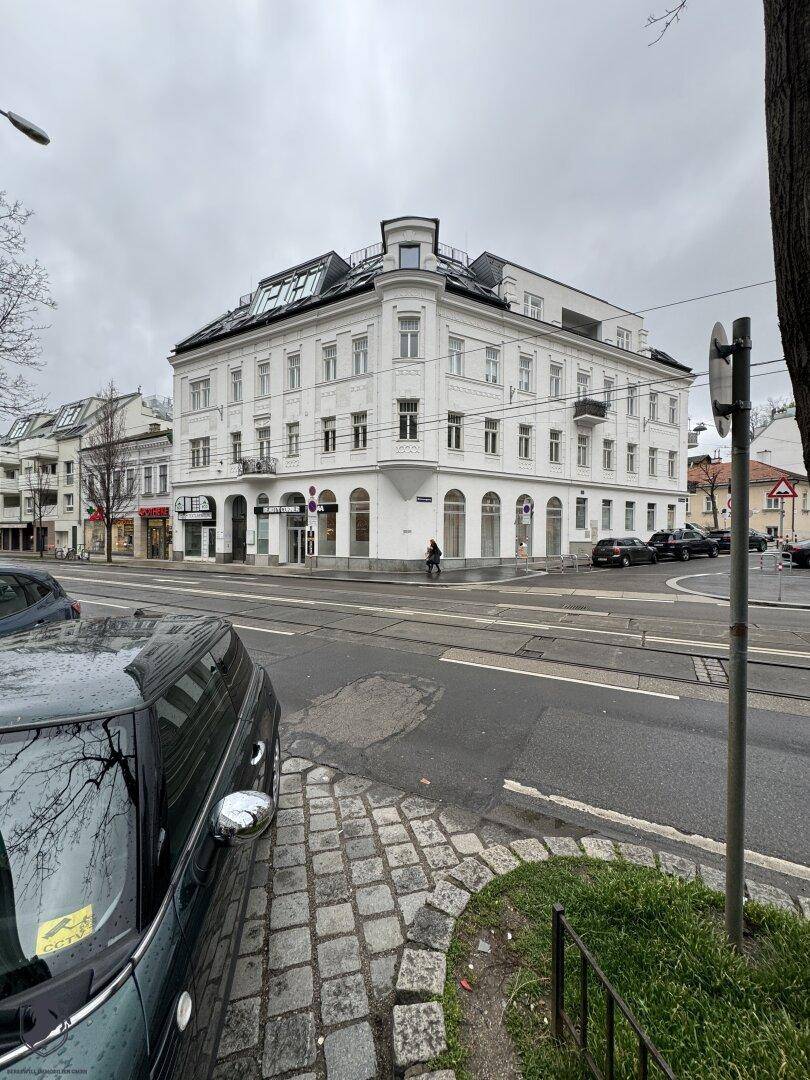 Historisches Eckgebäude mit weißer Fassade und modernen Dachaufbauten an einer städtischen Kreuzung.