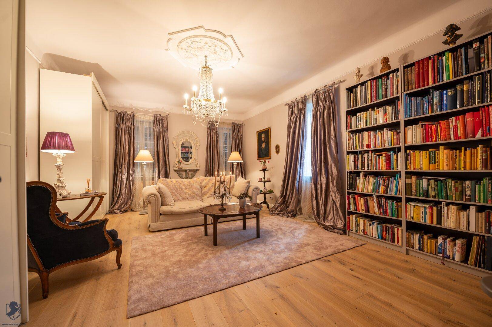 Elegantes Wohnzimmer mit großer Bücherwand, Kronleuchter und hellem Holzparkettboden.