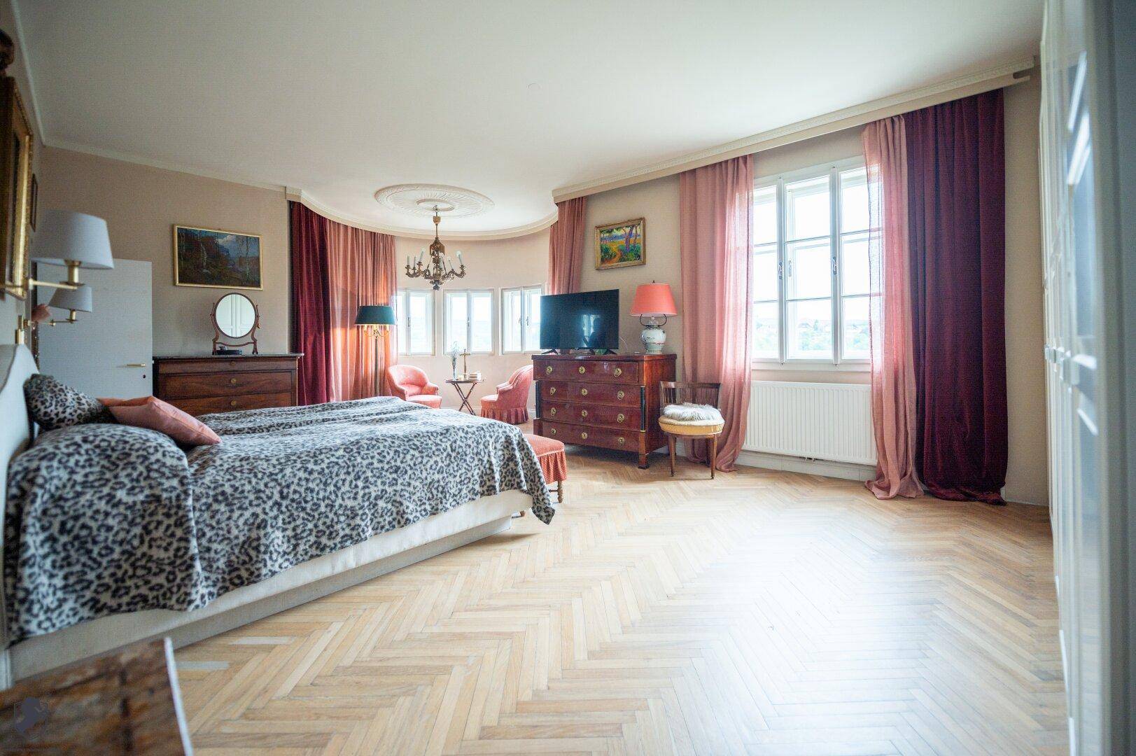 Geräumiges Schlafzimmer mit großem Bett, Kommode, Kronleuchter und hellem Fischgrätparkett.