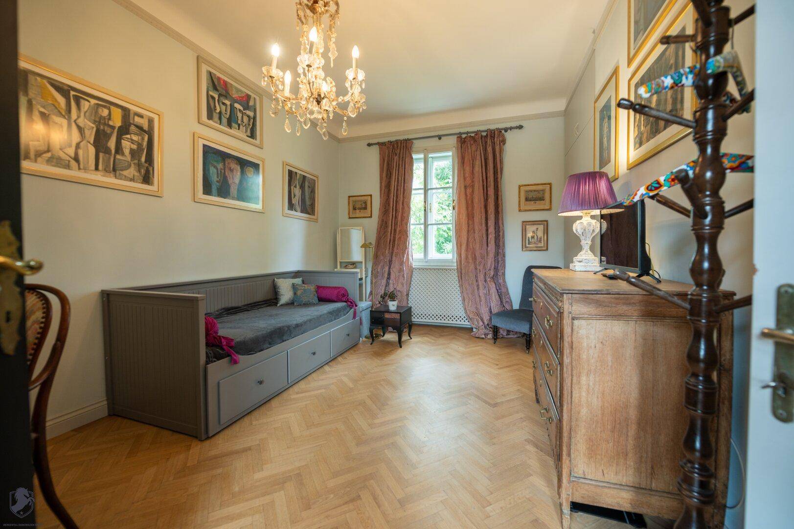 Helles Schlafzimmer mit Tagesbett, antiker Kommode, Kronleuchter und Fischgrätparkettboden.