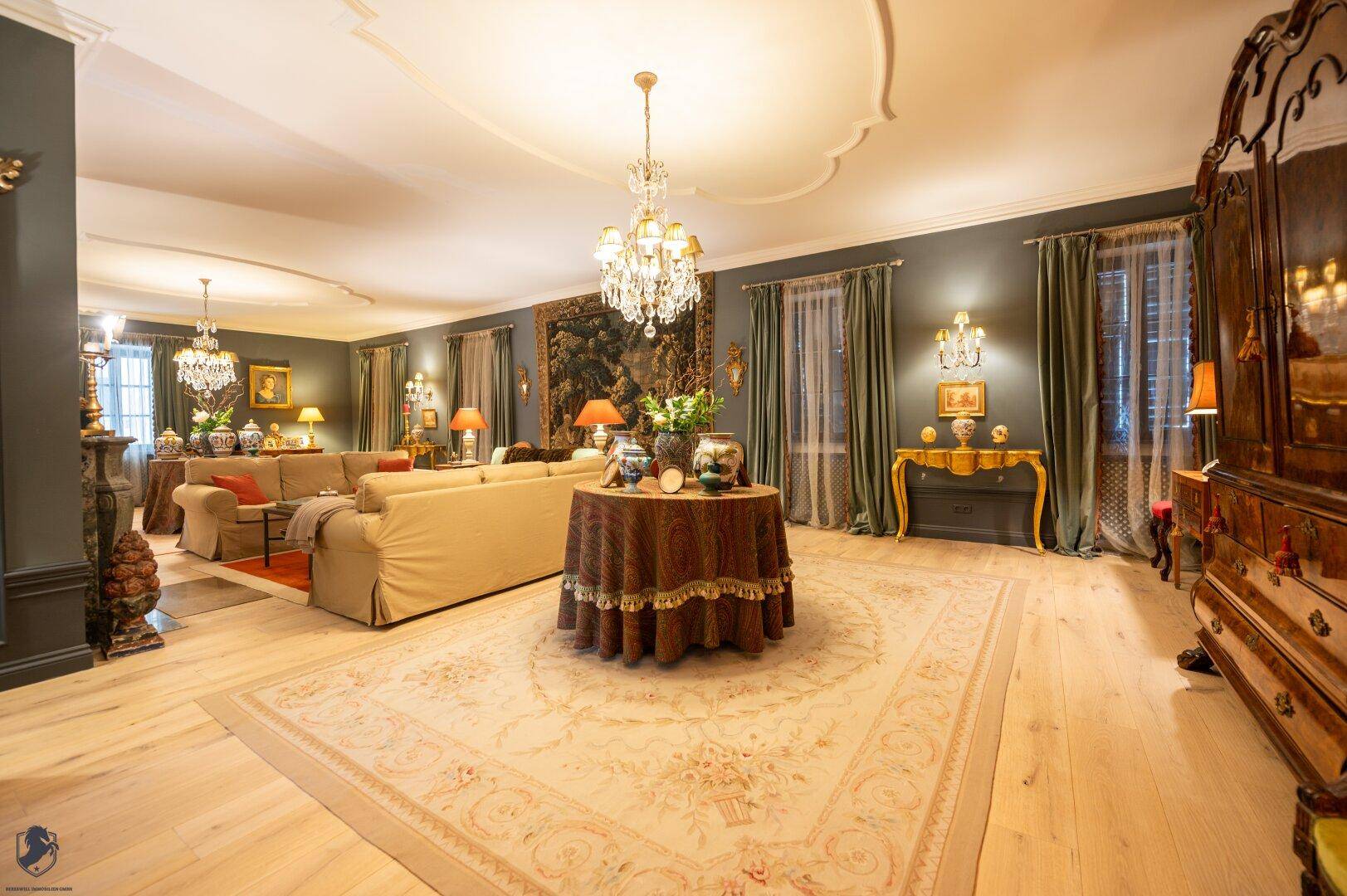 Großzügiges Wohnzimmer mit mehreren Sofas, Kronleuchter und elegantem Teppich auf Holzparkett.