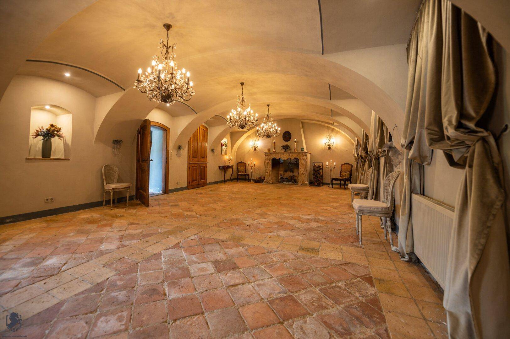 Historischer Gewölberaum mit Terrakottaboden, Kamin und eleganten Kronleuchtern.