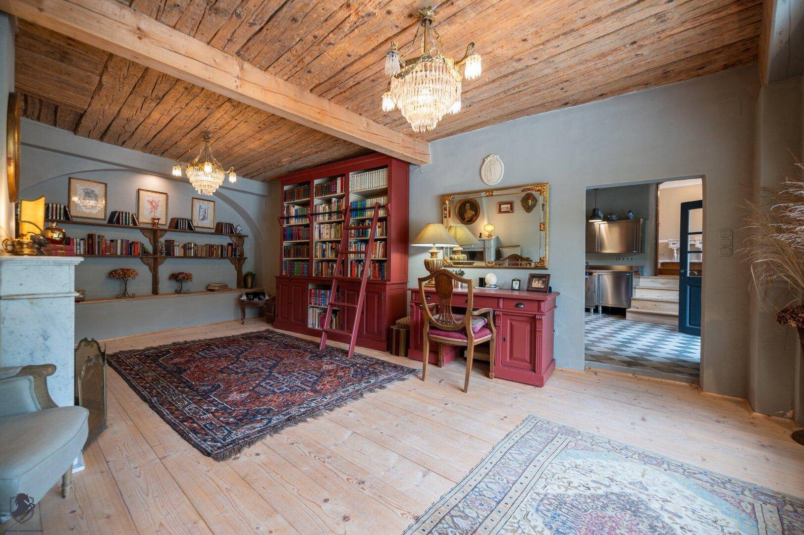 Arbeitszimmer mit sichtbaren Holzdeckenbalken, Bücherregalen, Schreibtisch und Kamin.