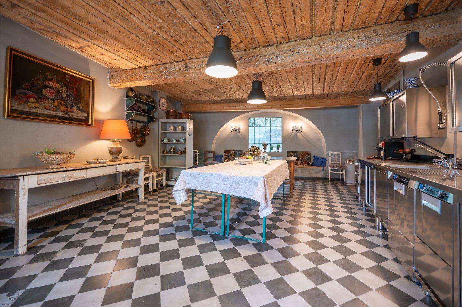 Geräumige Küche mit Edelstahl-Arbeitsflächen, Schachbrettmusterboden und rustikaler Holzdecke.