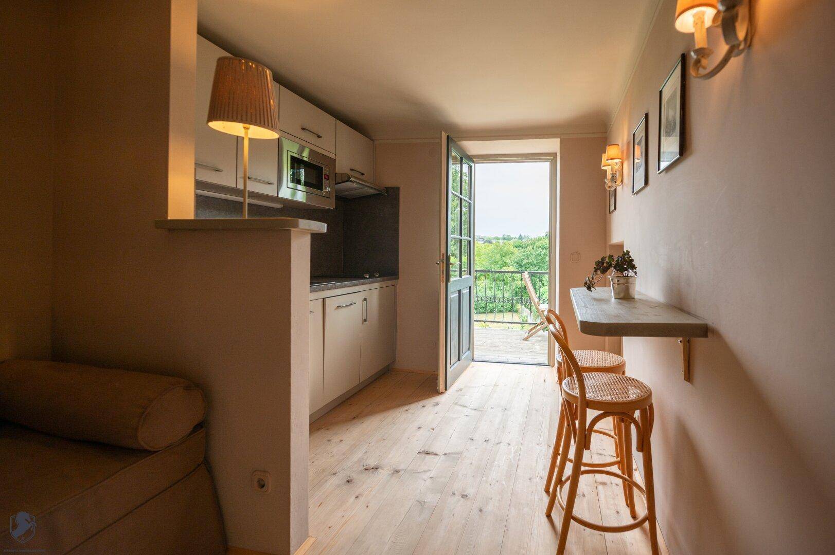 Kleine Küchenzeile mit Zugang zu einem Balkon und grünem Ausblick.