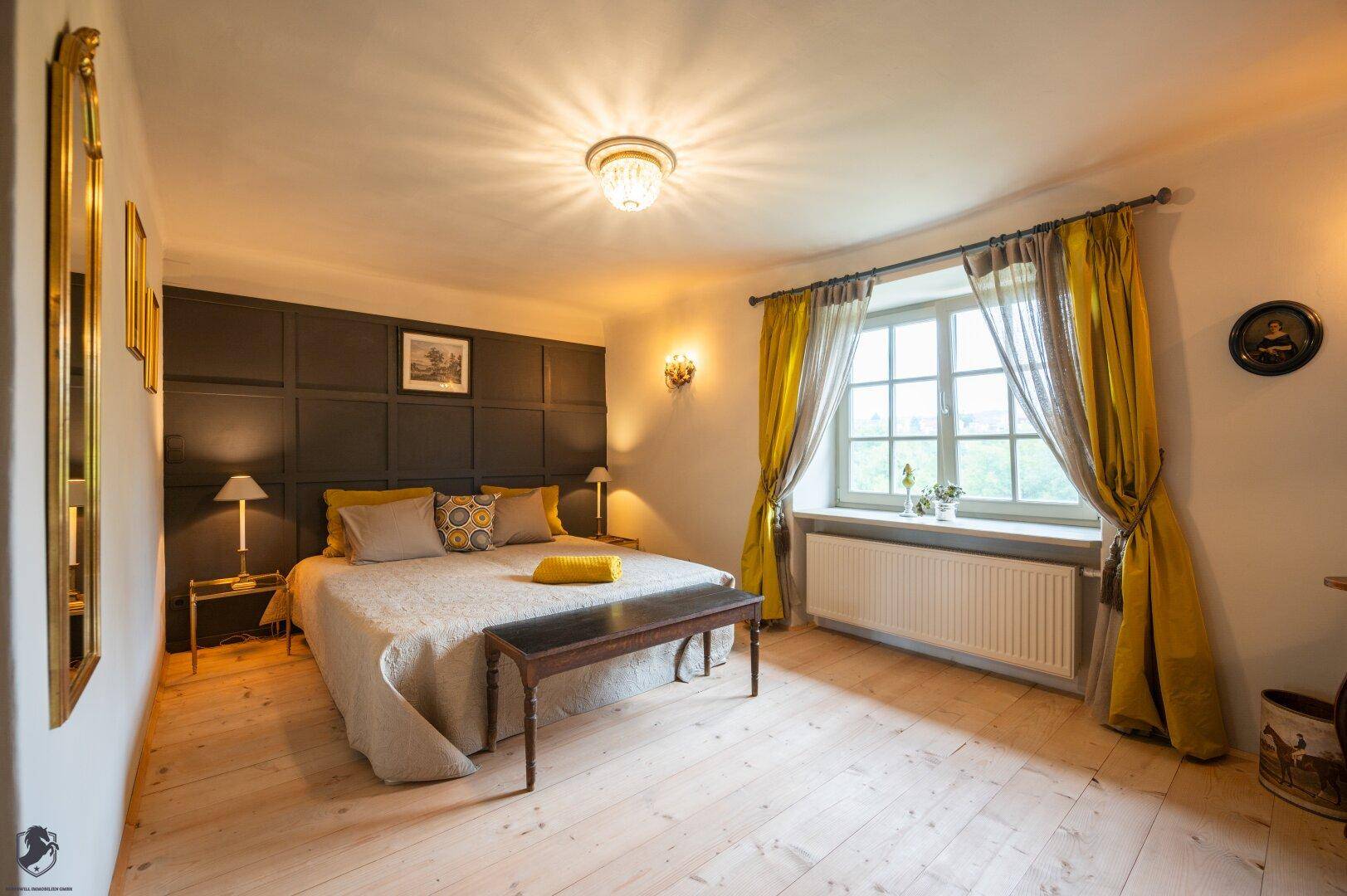 Schlafzimmer mit großem Bett, dunkler Akzentwand und hellem Holzplankenboden.