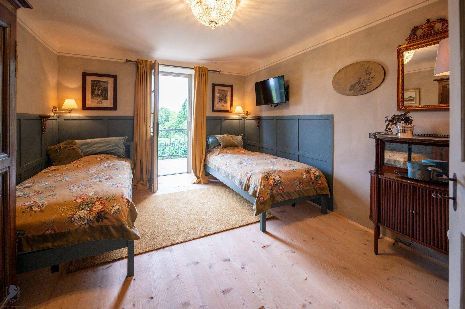 Schlafzimmer mit zwei Einzelbetten, Zugang zum Balkon und hellem Holzplankenboden.