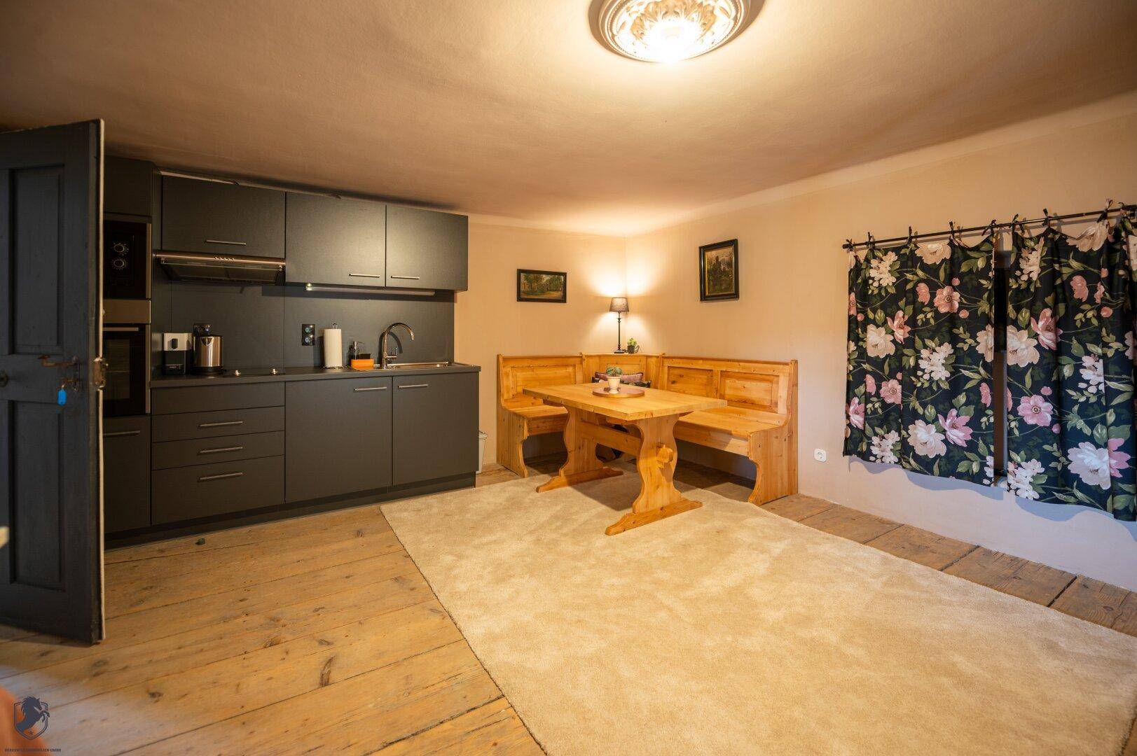 Küche mit dunklen Schränken, gemütlicher Essecke und rustikalem Holzplankenboden.