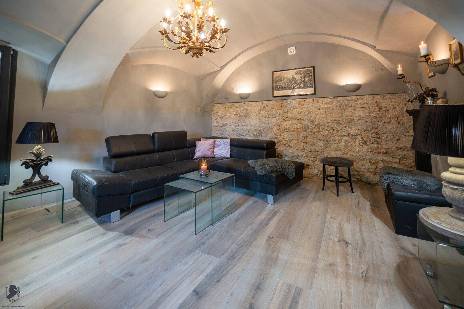 Modernes Wohnzimmer mit schwarzem Ledersofa, Gewölbedecke und freigelegter Steinwand.