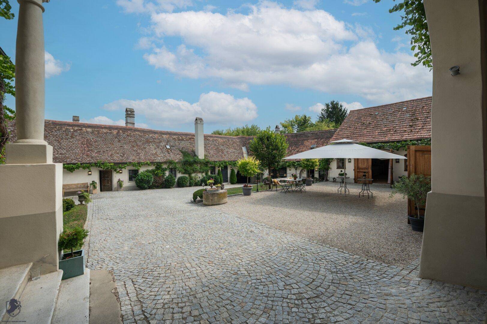 Historischer Innenhof mit Kopfsteinpflaster, Sitzgelegenheiten und einem alten Brunnen.