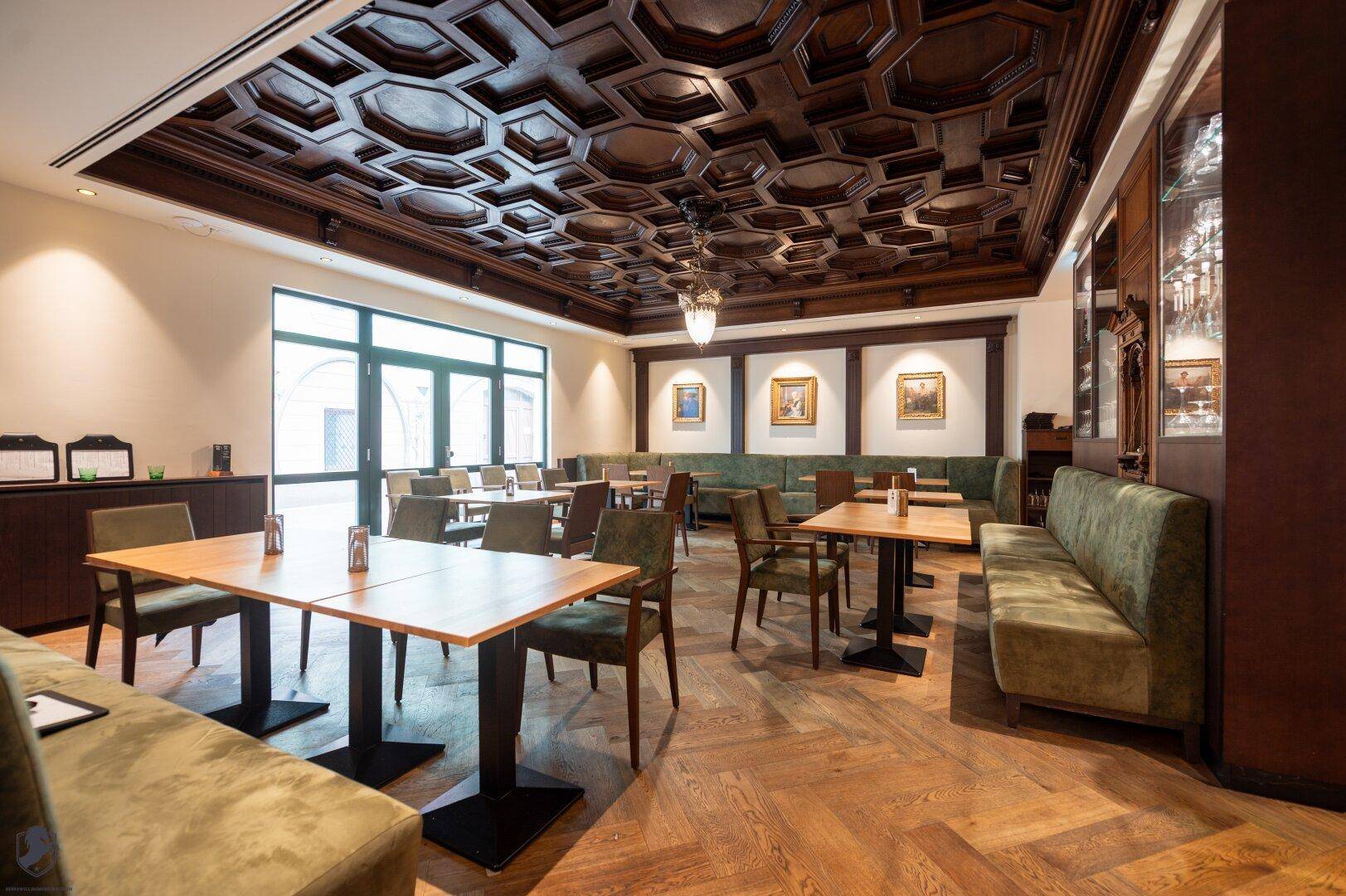Eleganter Speisesaal mit aufwendiger Holzdecke, Fischgrätparkett und bequemen Sitzbänken.