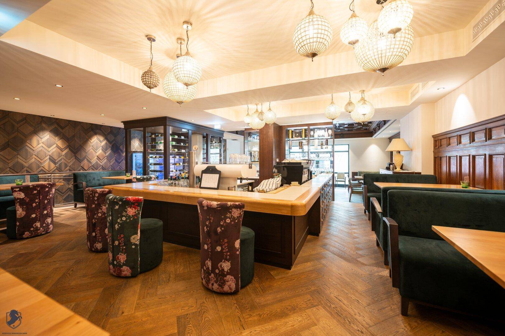 Gemütlicher Barbereich mit Holzboden, eleganten Kronleuchtern und floral gemusterten Hockern.