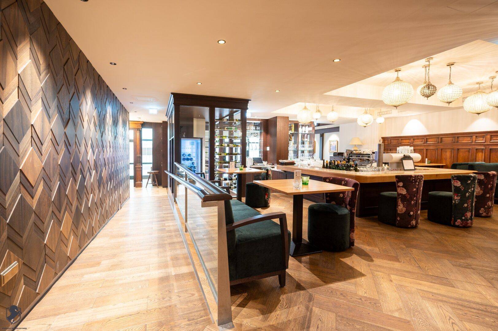 Langer Flur mit Holzwandverkleidung, Fischgrätparkett und Blick auf den Barbereich.