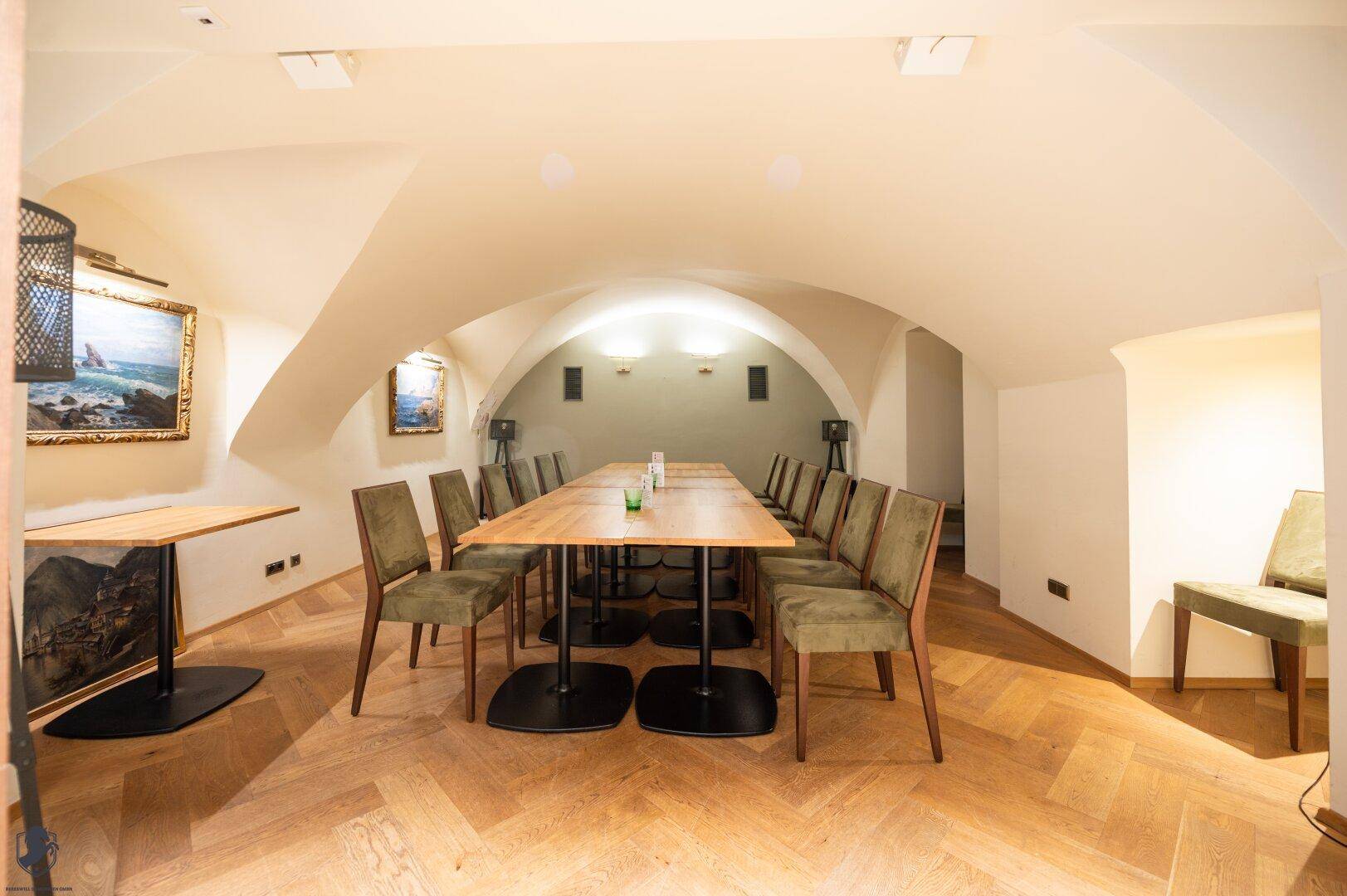 Gewölbter Speisesaal mit Holzboden, langer Tafel und Kunstwerken an den Wänden.