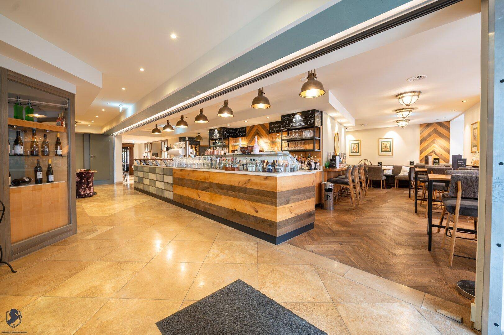 Geräumiger Restaurantbereich mit Theke, Steinboden und Übergang zu weiteren Sitzbereichen.