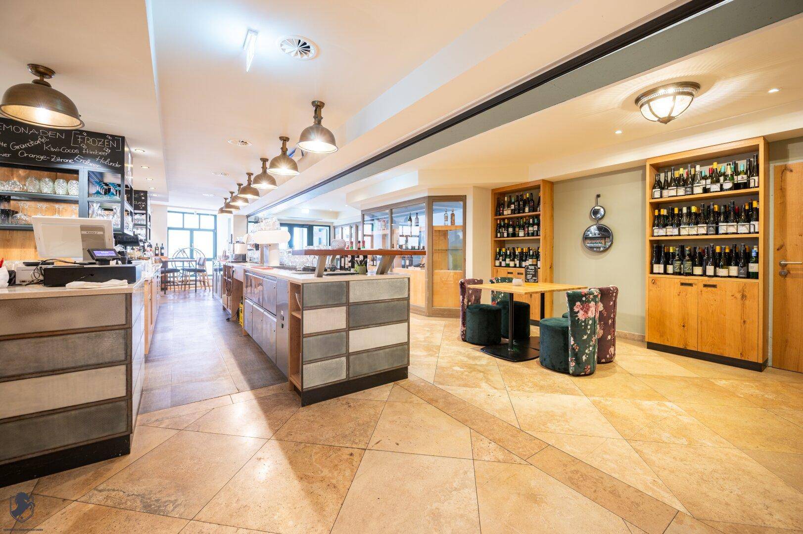 Offener Restaurantbereich mit Theke, Steinboden und Weinschränken im Hintergrund.