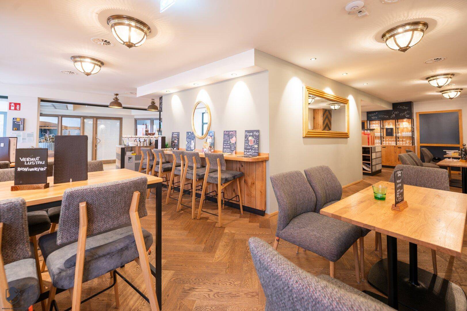 Gemütlicher Restaurantbereich mit Holzboden, Barhockern und Spiegeln an der Wand.