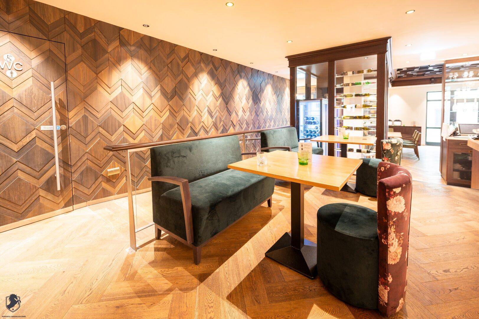 Gemütlicher Sitzbereich mit Holzboden, grünen Sofas und dekorativer Holzwand.