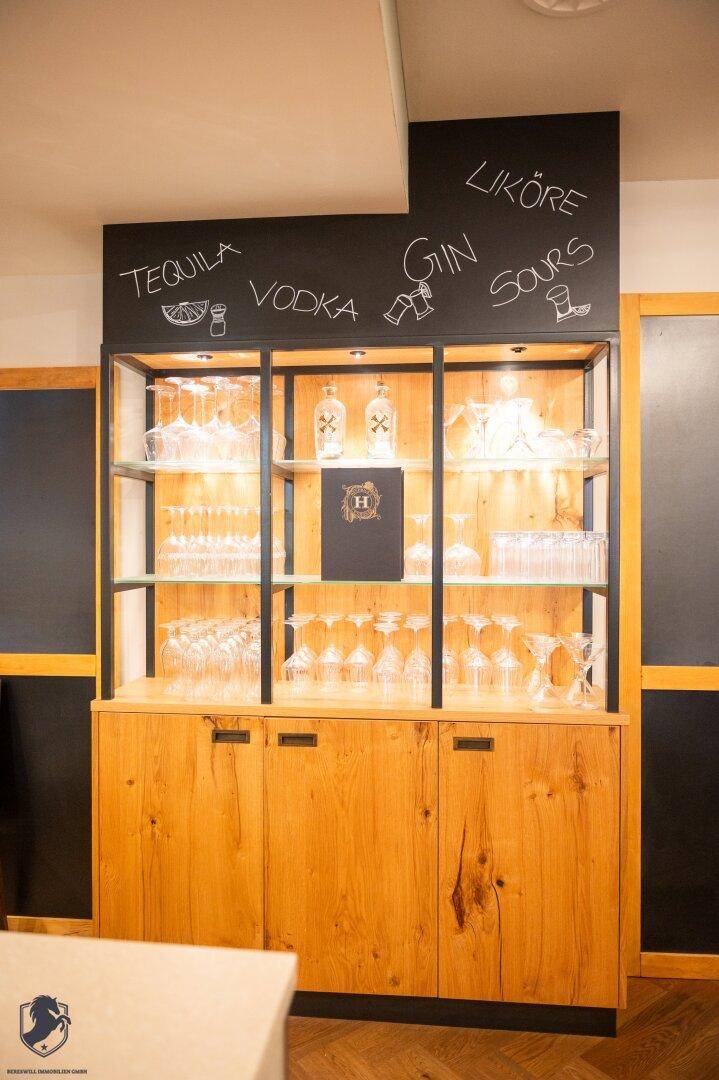 Holzschrank mit beleuchteten Glasregalen und einer Kreidetafel mit Getränkeangeboten.