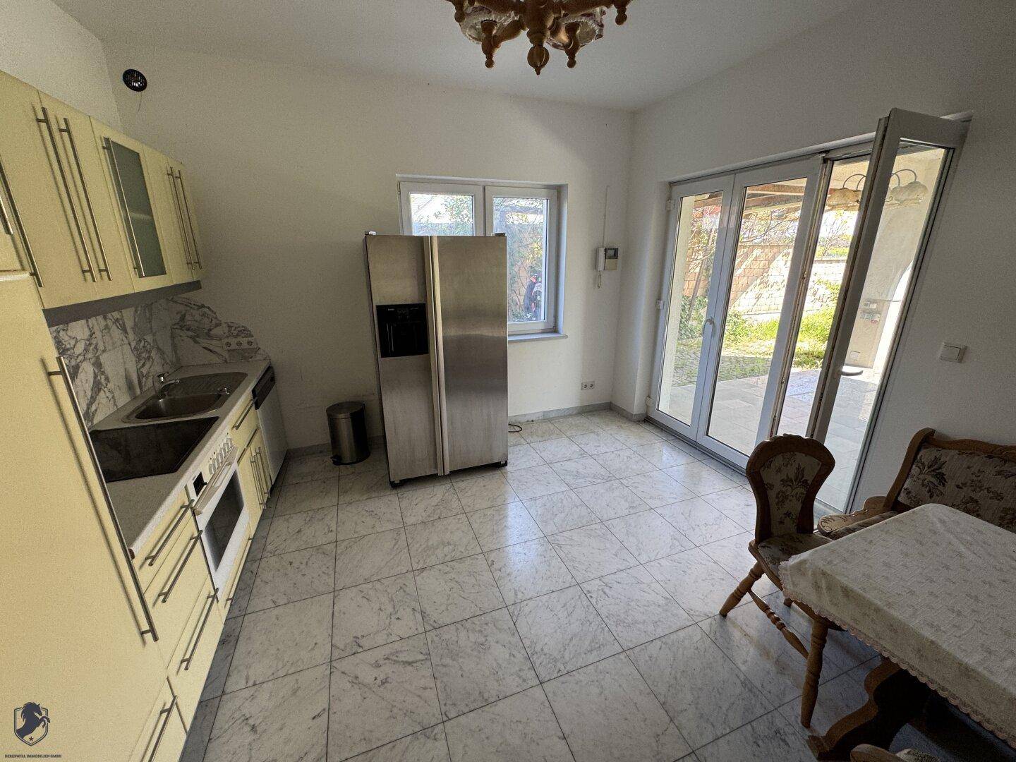 Geräumige Küche mit Fliesenboden, großem Kühlschrank und Zugang zu einem Außenbereich.