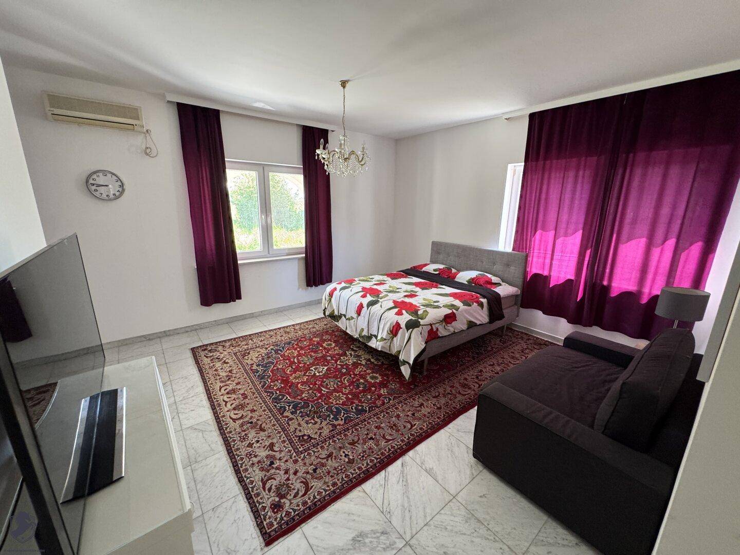 Helles Schlafzimmer mit großem Bett, Sofa, Teppich und Klimaanlage.