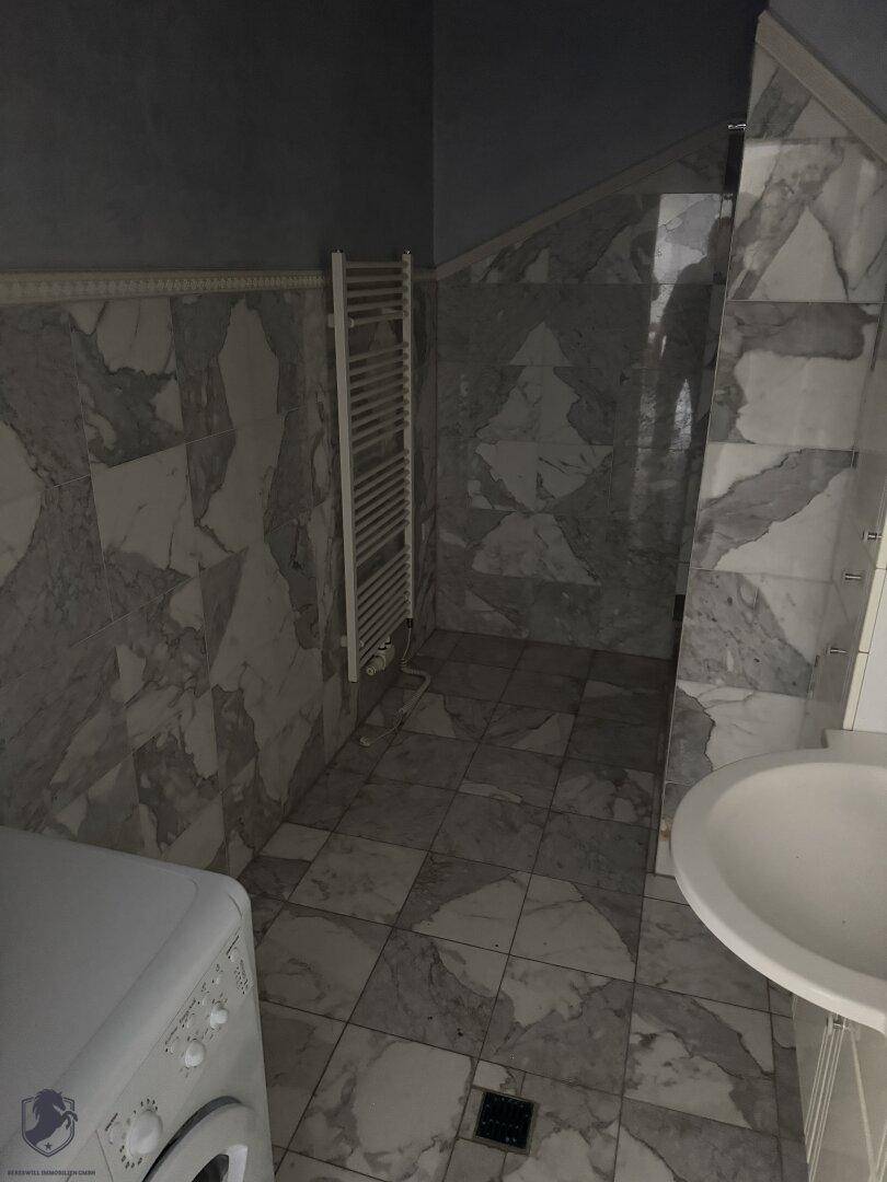 Badezimmer mit Marmorfliesen, Waschmaschine, Waschbecken und beheiztem Handtuchhalter.