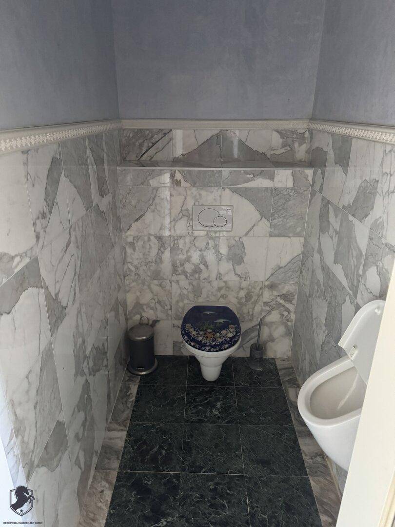 Separate Toilette mit Marmorwandfliesen und dunklem Boden, ausgestattet mit zwei WCs.