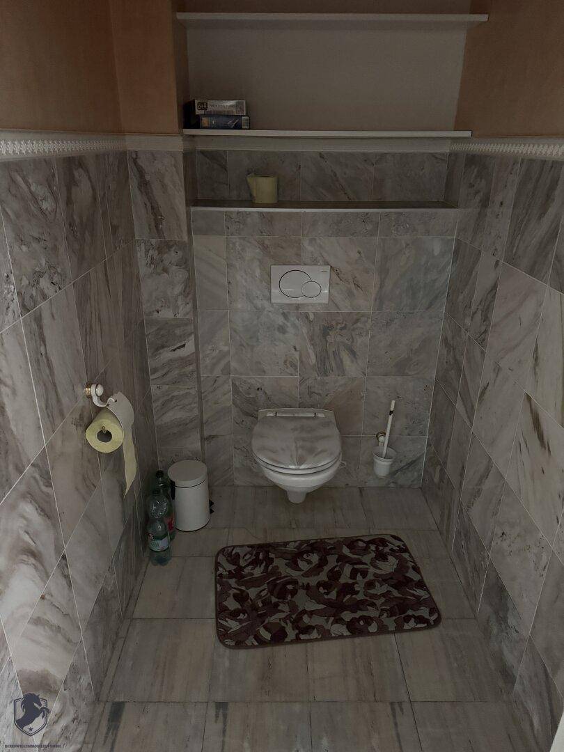 Separate Toilette mit Marmorwandfliesen und hellem Boden, ausgestattet mit einem WC.