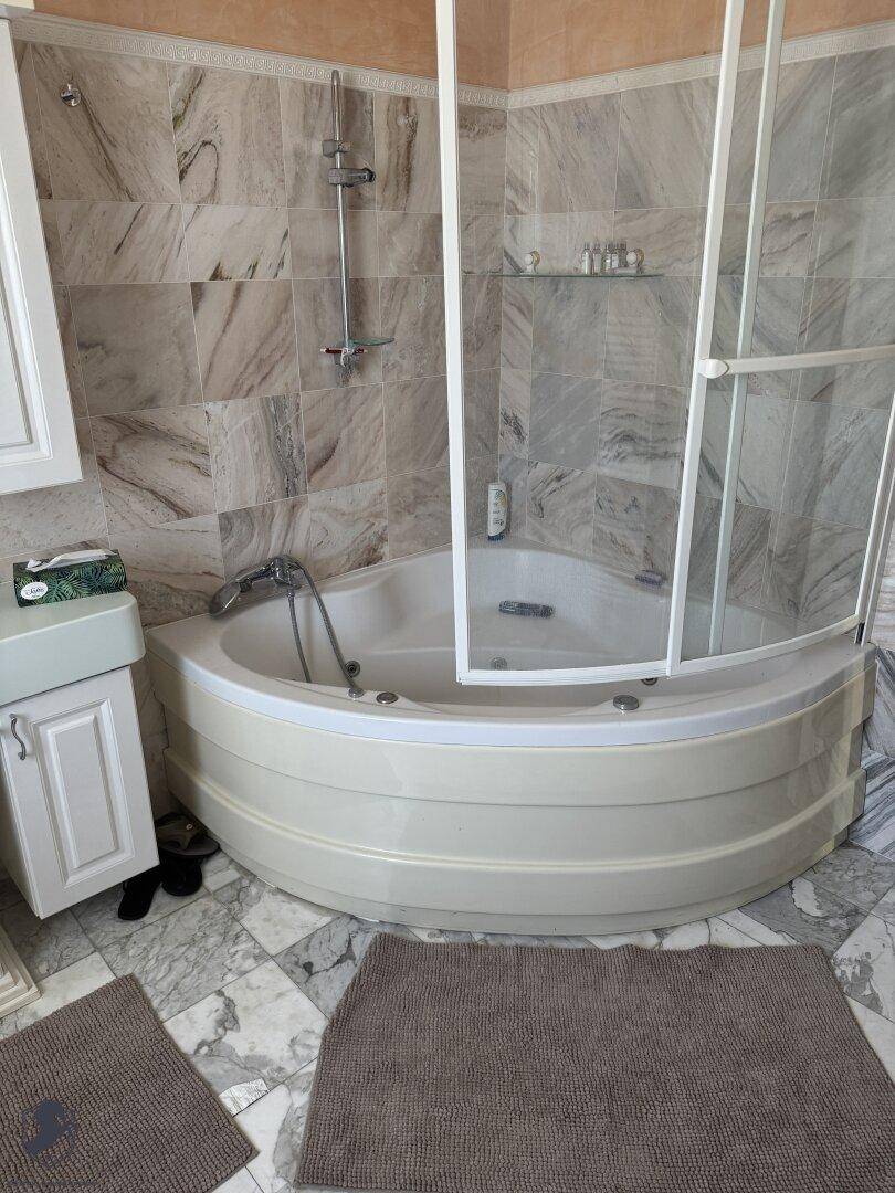 Badezimmer mit Eckbadewanne, Duschabtrennung und Marmorfliesen an Wänden und Boden.