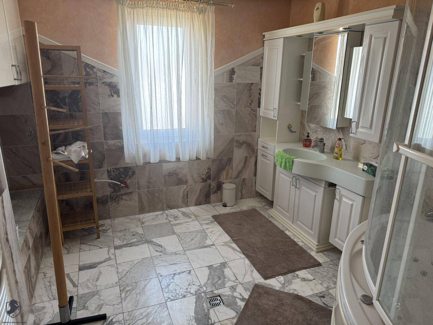 Geräumiges Badezimmer mit Marmorfliesen, großem Fenster, Waschtisch und Spiegelschrank.