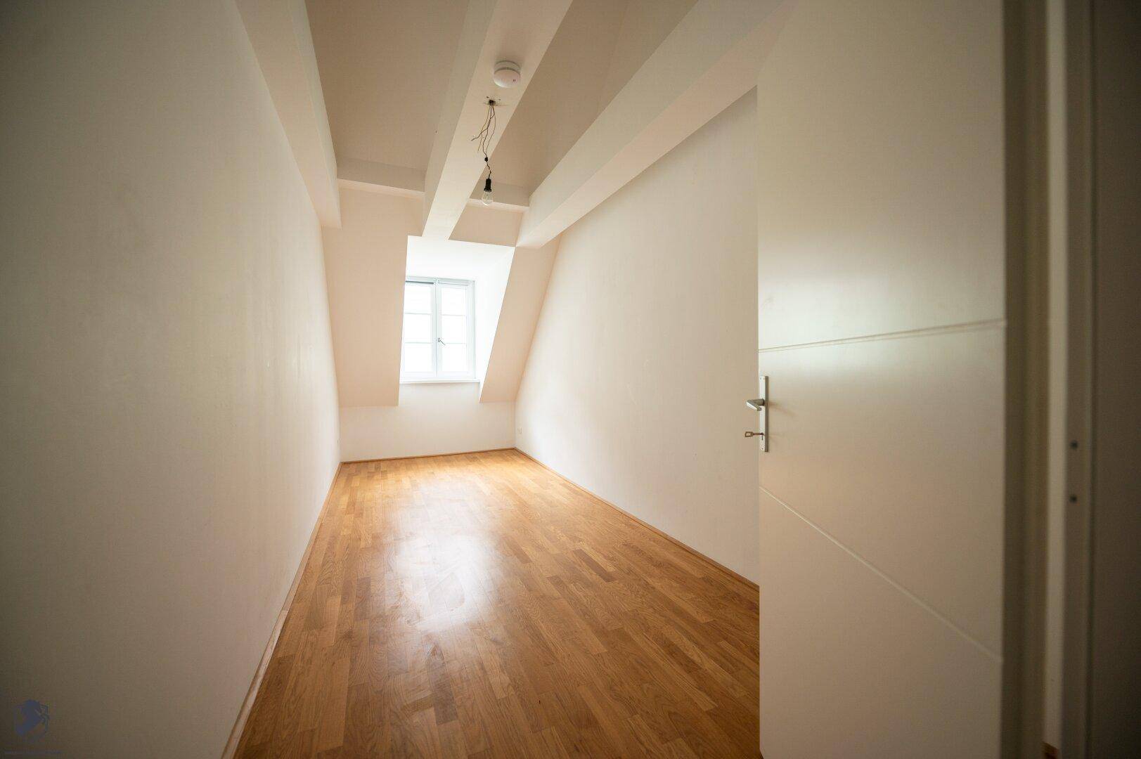 Kleinerer Raum mit Holzboden, weißen Wänden und schrägen Decken im Dachgeschoss, ideal als Schlafzimmer.