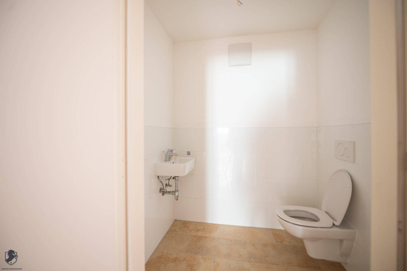 Modernes Gäste-WC mit wandhängender Toilette, kleinem Waschbecken und hellen Fliesen.