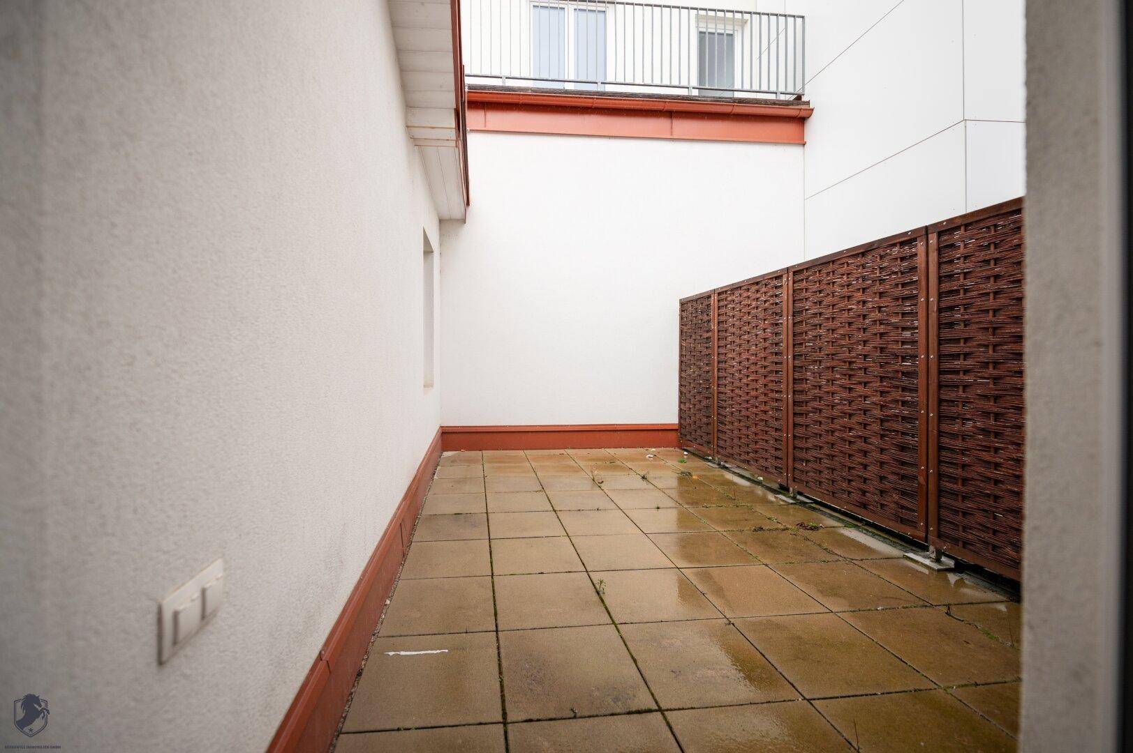 Außenbereich mit gefliester Terrasse und einem Sichtschutz aus Holz.