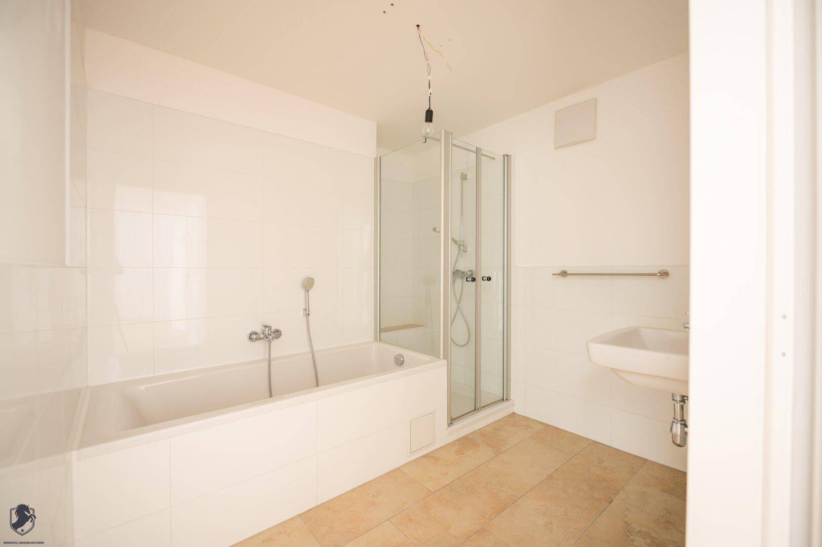 Badezimmer mit Badewanne, Duschkabine, Waschbecken und hellen Fliesen an Boden und Wänden.