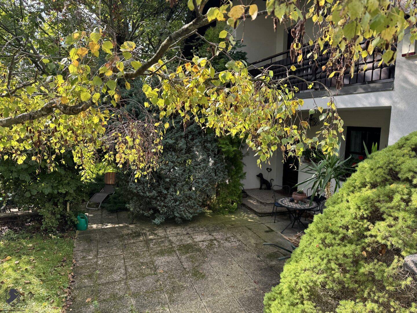 Gemütliche gepflasterte Terrasse mit Gartenmöbeln und üppiger Bepflanzung am Haus.