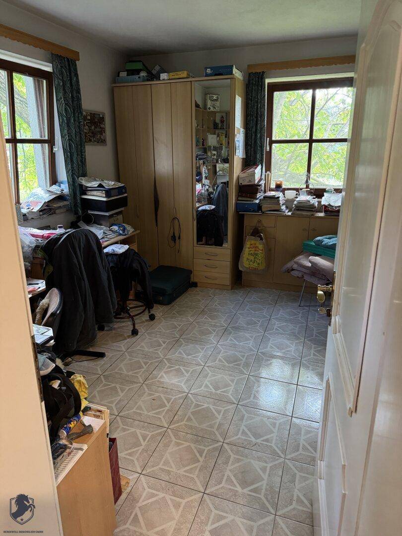 Gemütliches Schlafzimmer mit zwei Fenstern, Holzschrank und gemustertem Fliesenboden.
