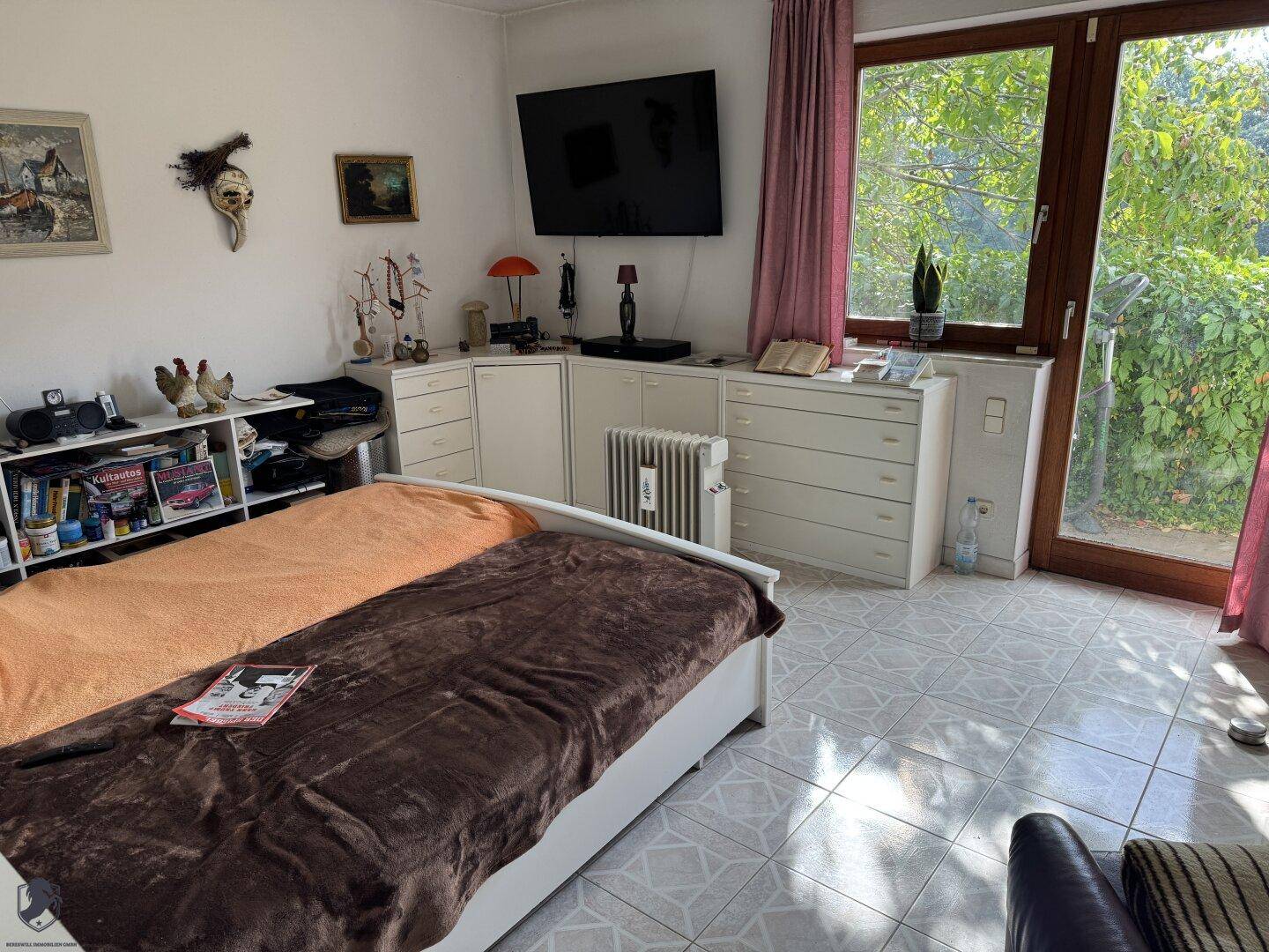 Helles Schlafzimmer mit großem Fenster, Fliesenboden und Blick ins Grüne.