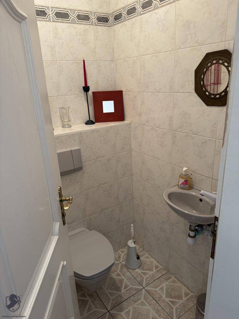 Kleines Gäste-WC mit hellen Fliesen, Wand-WC und kleinem Waschbecken.