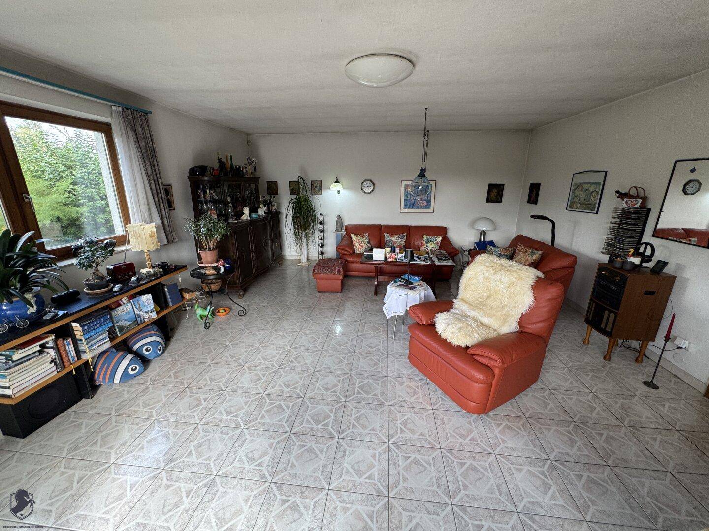 Geräumiges Wohnzimmer mit Fliesenboden, roten Ledermöbeln und Blick in den Garten.