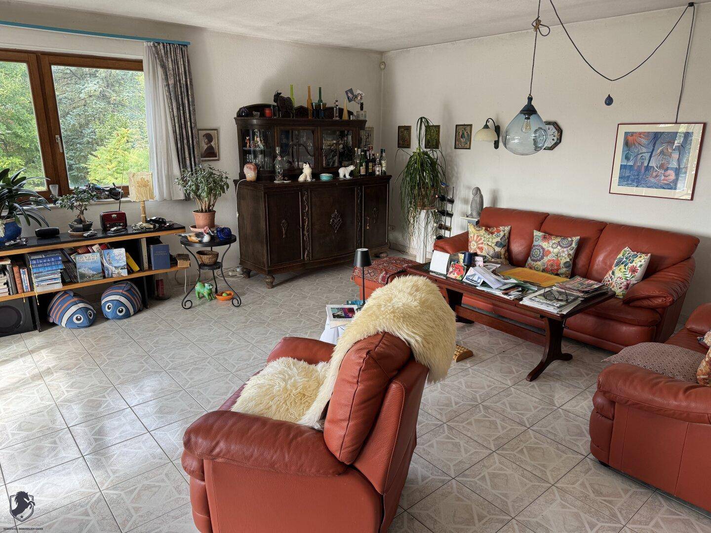 Wohnzimmer mit bequemen Ledersofas, Fliesenboden und Fenster zum grünen Außenbereich.
