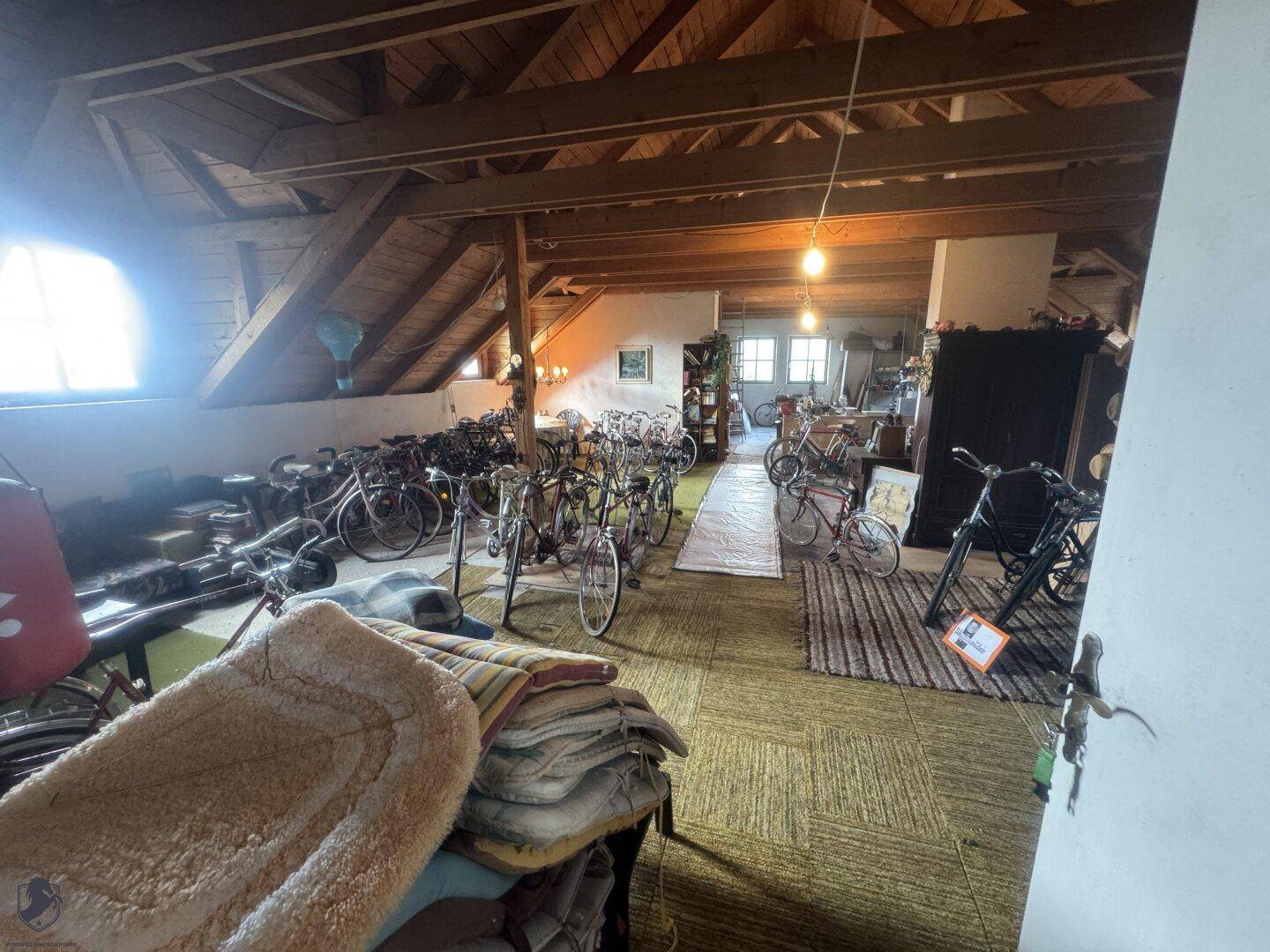 Geräumiger Dachboden mit sichtbaren Holzbalken, Teppichboden und vielen Fahrrädern.